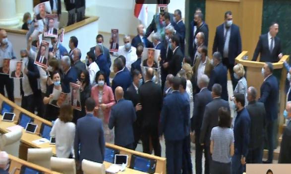 პარლამენტში ვახტანგ გომელაურის სიტყვით გამოსვლის დაწყება ვერ ხერხდება - ოპოზიციონერი დეპუტატები შს მინისტრის ტრიბუნასთან პლაკატებით მივიდნენ