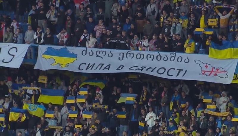 "ძალა ერთობაშია" - ქართველი და უკრაინელი გულშემატკივრის საერთო ბანერი მატჩზე, ქართული და უკრაინული წარწერით, ორი ქვეყნის რუკითა და დროშებით